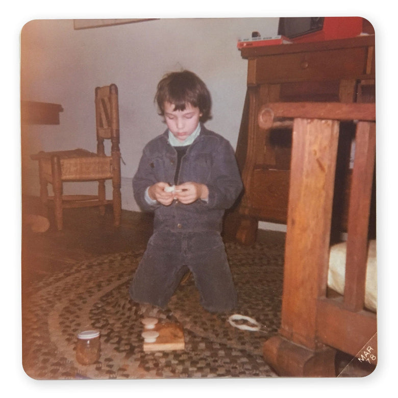 Small boy kneeling on a braided rug making something out of a piece of wood, some wooden knobs, and yarn. 